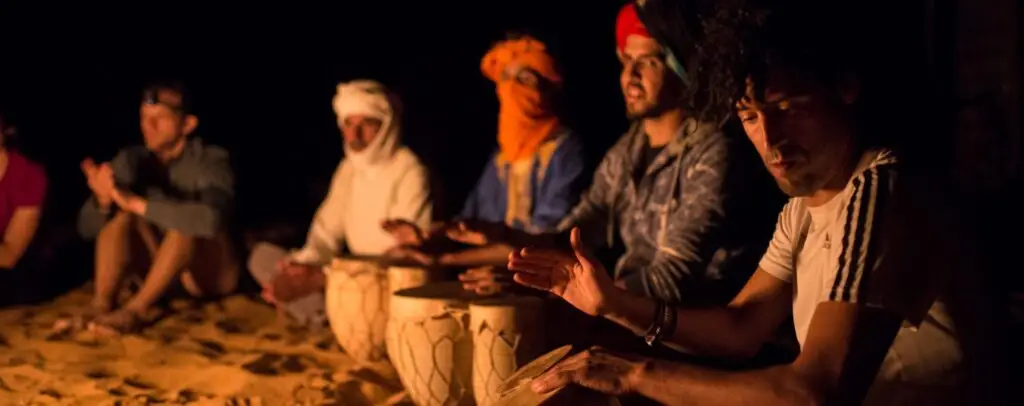 Desert camp cultural experience: locals and travelers play traditional drums by firelight.