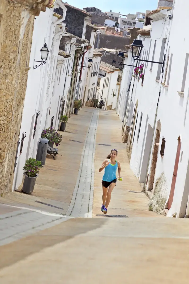 A runner climbing a narrow white-walled street in a Costa Brava village