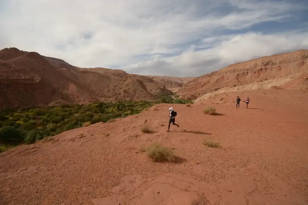 Two runners crossing a red desert plateau in Morocco