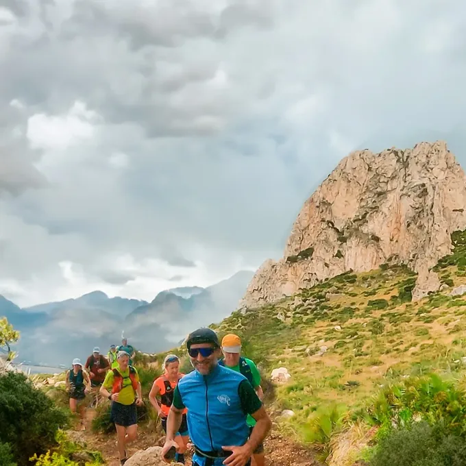 The group running a hillside trail with Monte Cofano behind them